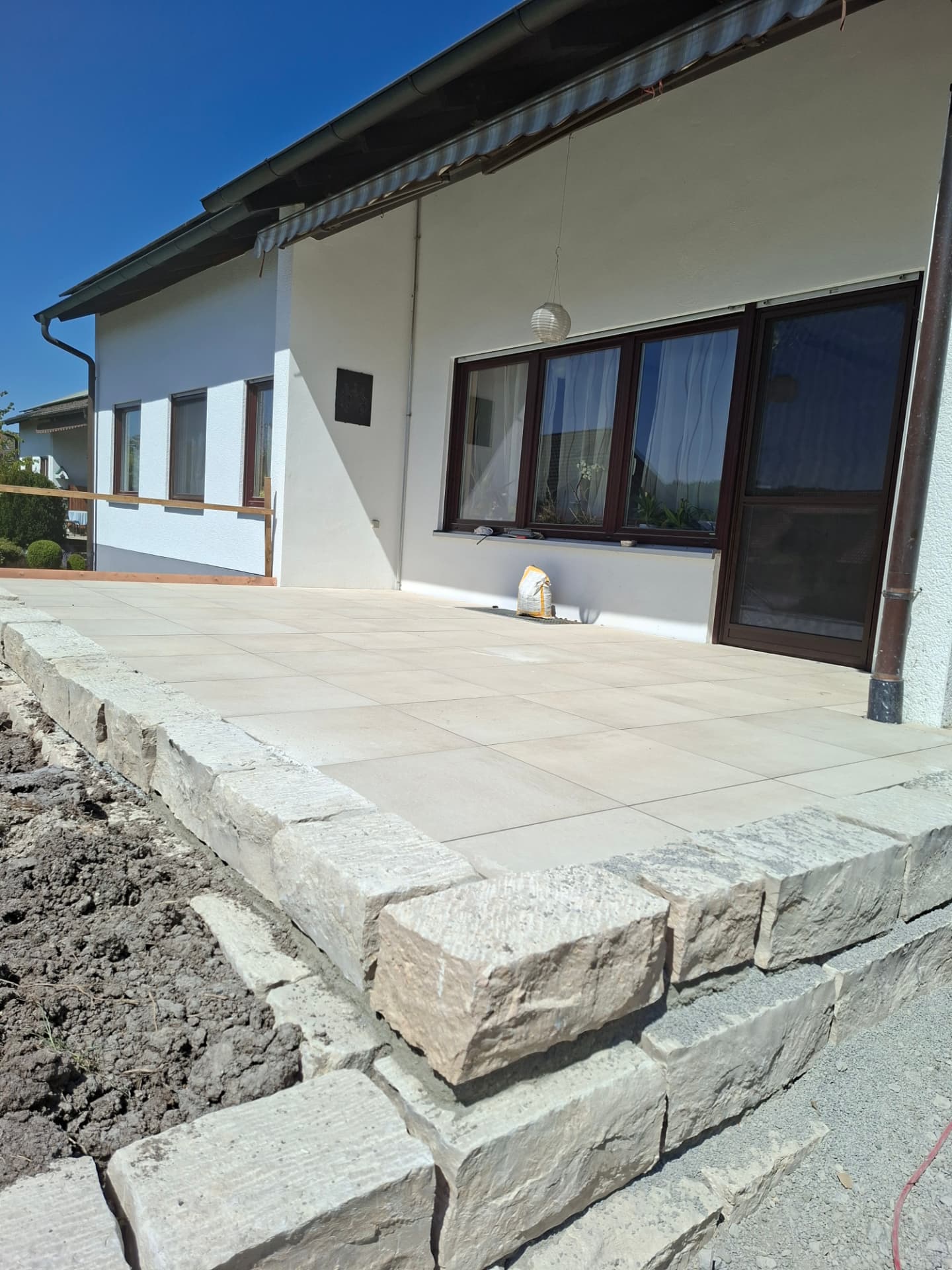Neue Terrasse mit großformatigen Platten und Blocksteineinfassung an einem Wohnhaus