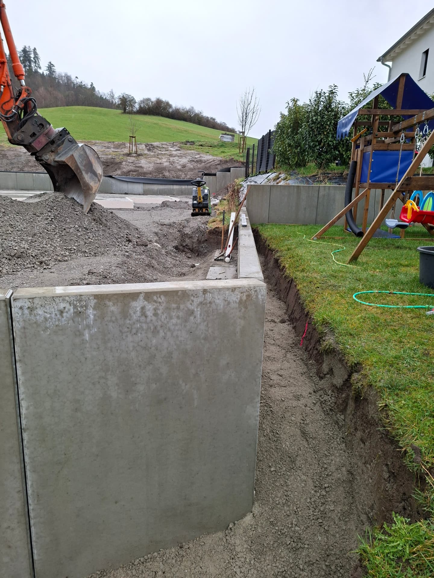 Betonstützwände fangen einen Geländesprung neben einem Garten mit Spielgerät ab